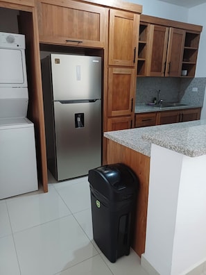 Eine Küche mit Holzausstattung, einem Edelstahlkühlschrank, einer Spüle und einem Mülleimer.