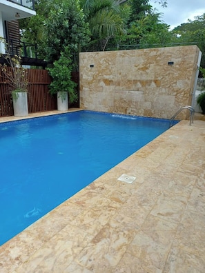 A rectangular swimming pool with a blue interior, surrounded by a stone wall and a wooden fence. - Sunrise: 3 Queen Bedrooms, Upstairs Lounge, Pool & Beach Nearby (Puerto Plata)