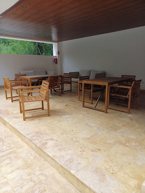 A spacious room with a high ceiling and a stone floor, furnished with wooden tables and chairs. - Sunrise: 3 Queen Bedrooms, Upstairs Lounge, Pool & Beach Nearby (Puerto Plata)