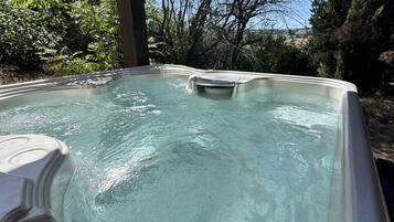 Ett bubbelbad med klart vatten, omgivet av träd och en klar himmel.