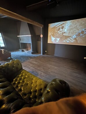 A room with a dark-colored leather sofa, a fireplace, and a large screen displaying a person playing a guitar. - defaultName (Lacroix-Falgarde)