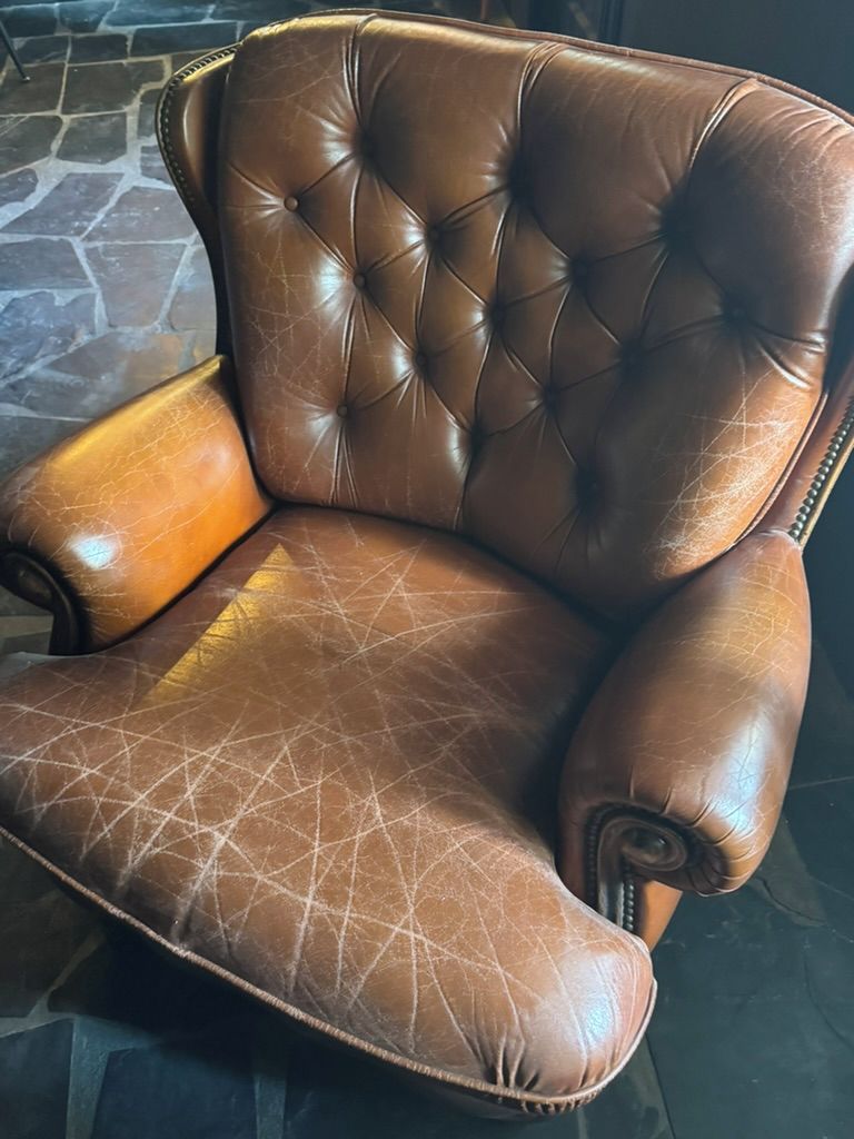 A brown leather armchair with a tufted backrest and armrests.