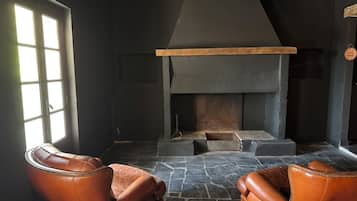 A room with a fireplace, two leather armchairs, and a stone floor.