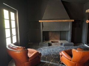 A room with a fireplace, two leather armchairs, and a stone floor. - defaultName (Lacroix-Falgarde)