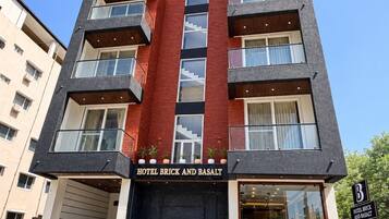 A multi-story hotel with a prominent red and grey facade, balconies on each floor, and a clear entrance.