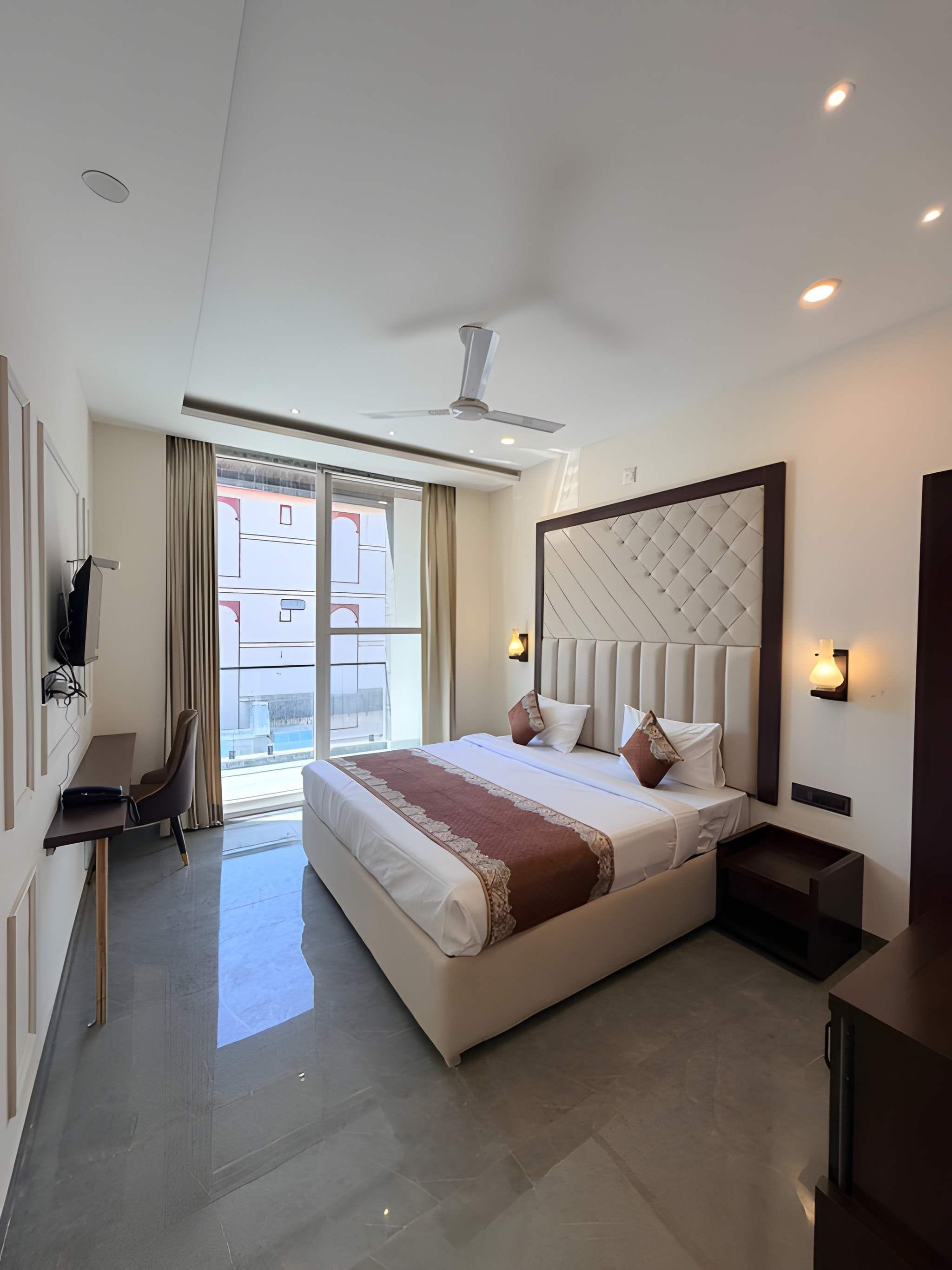 A modern hotel room with a large bed, a desk, a chair, and a view of the outside.