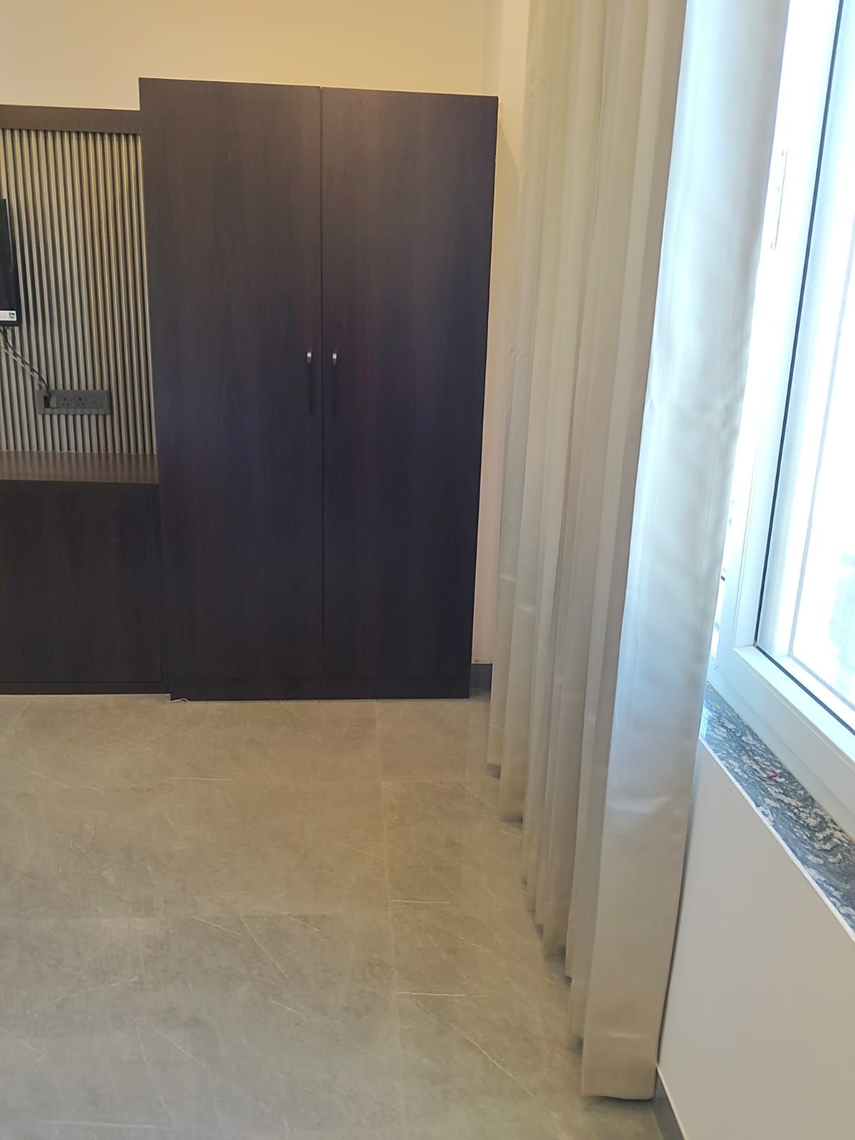 Una habitación con un armario de madera oscura, suelo de baldosas y una ventana con cortinas.