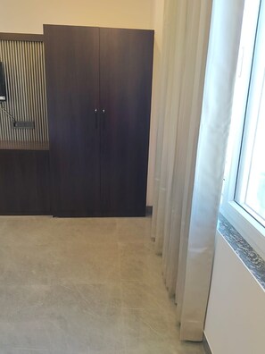 Una habitación con un armario de madera oscura, suelo de baldosas y una ventana con cortinas.