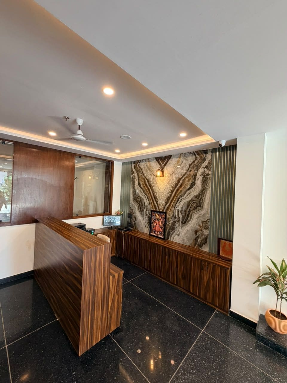 A reception desk with a marble wall backdrop, a ceiling fan, and a potted plant.