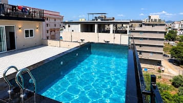 A rooftop swimming pool with clear blue water, surrounded by a black pool deck and a metal railing.