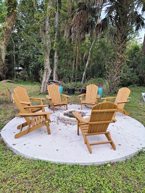 A circular seating arrangement with wooden chairs around a central fire pit, surrounded by greenery. - Charming Cottage 1.5 miles from historic St. Augustine (St. Augustine)
