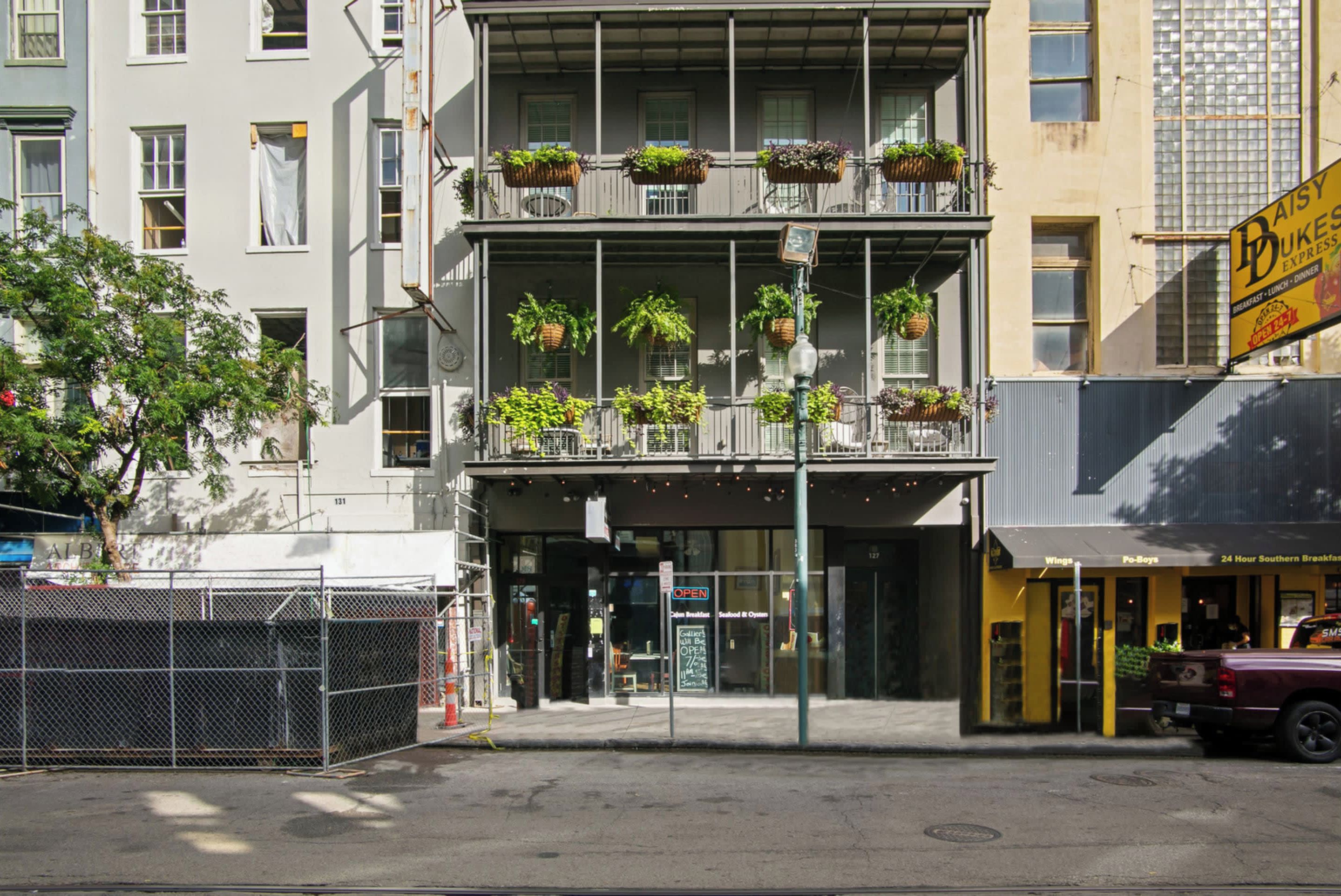 Ein mehrstöckiges Gebäude mit Eingang im Erdgeschoss, einem Balkon mit hängenden Pflanzen und einem sichtbaren Schild für Daisy Buksen Express.