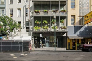 Ein mehrstöckiges Gebäude mit Eingang im Erdgeschoss, einem Balkon mit hängenden Pflanzen und einem sichtbaren Schild für Daisy Buksen Express.