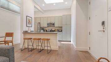Een moderne keuken met een centraal eiland, barkrukken en een zithoek met een grijze bank.