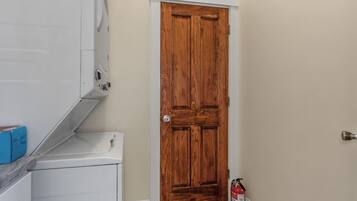 A laundry room with a white washer and dryer, a wooden door, and a fire extinguisher.