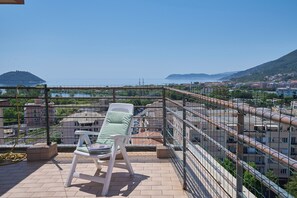 A balcony with a white chair, a view of the sea, and buildings in the background. - Tra le Nuvole (Albenga)