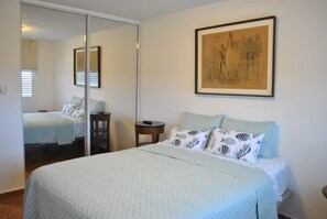 Ein Schlafzimmer mit Bett, Nachttisch, Stuhl, Spiegel und einem Bild an der Wand.