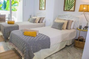 A hotel room with two beds, each with patterned bedding and pillows, a small table with a lamp, and a view of greenery outside. - BenalGolf 2H Apartment with Terrace and Pools (Benalmádena)
