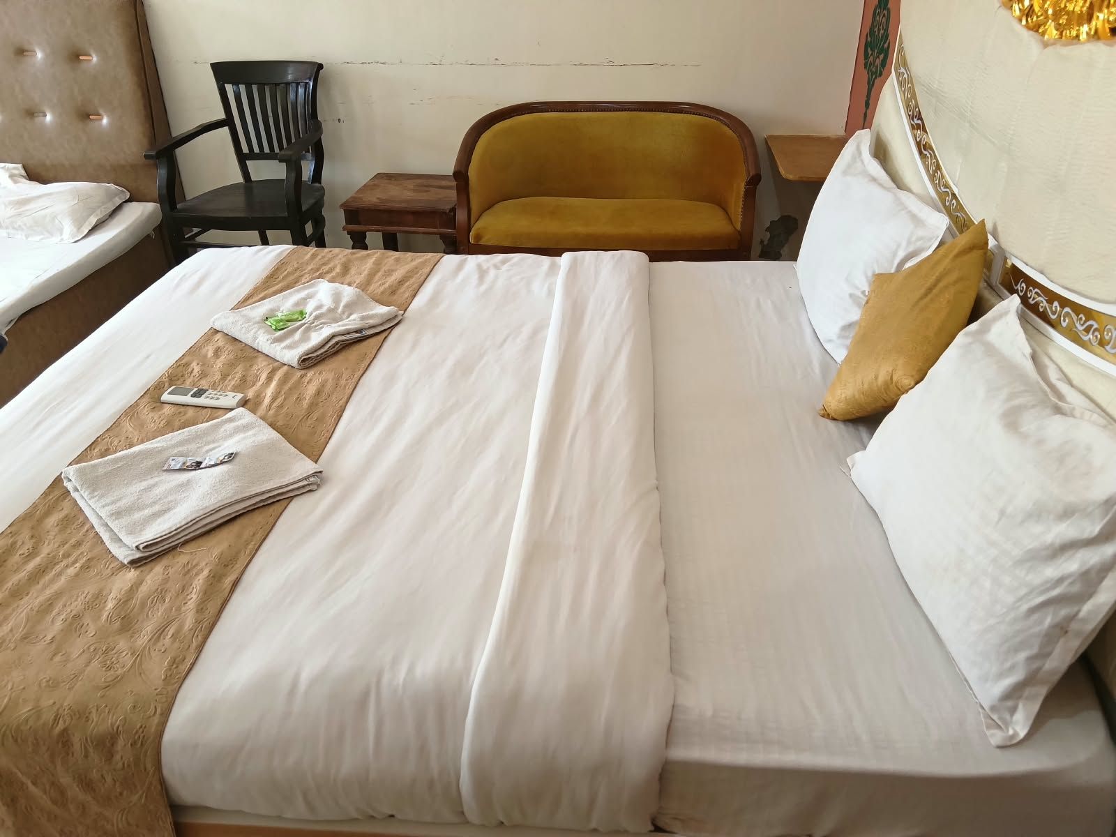 Una cama bien hecha con sábanas blancas, un cabecero de madera y una pequeña mesa de madera con una silla a un lado.
