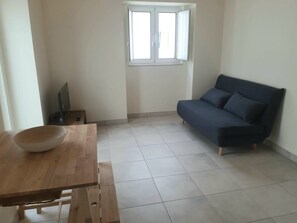 A room with a wooden table, a dark sofa, and a window with blinds. - Charming studio with a mezzanine and a courtyard with a lemon tree—a 5-minute walk to the old town (Faro)