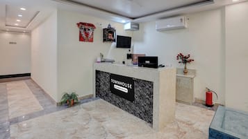 Un espace d’accueil doté d’un sol en marbre, d’un comptoir de réception, d’un ventilateur de plafond, de climatiseurs muraux et d’un extincteur.
