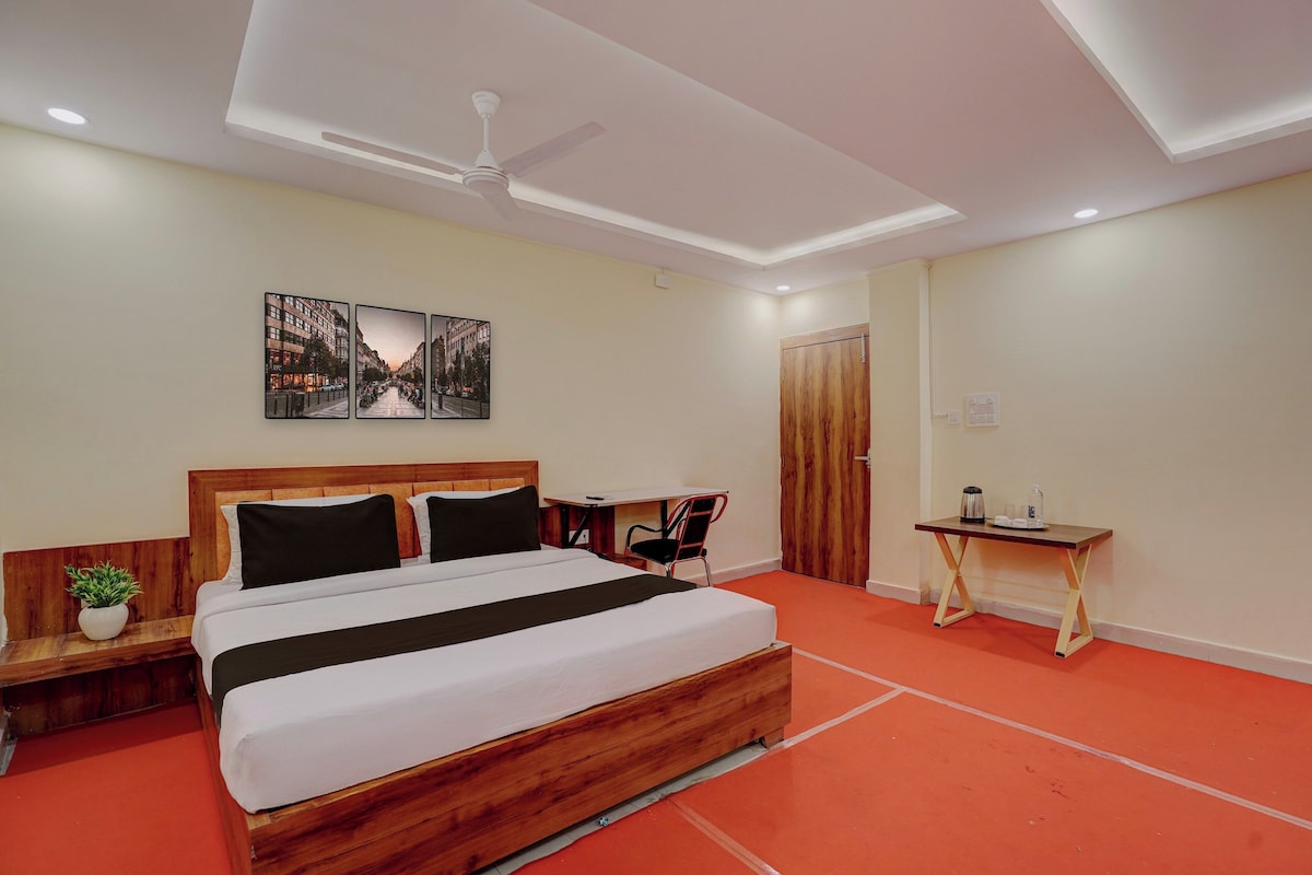 Habitació d'hotel amb un llit de fusta, escriptori, cadira, ventilador de sostre i una obra d'art penjada a la paret.