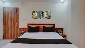 Una habitación de hotel con cabecera de madera, cama con ropa de cama blanca y negra, mesita de noche con teléfono y planta, y tres piezas de arte abstracto en la pared.