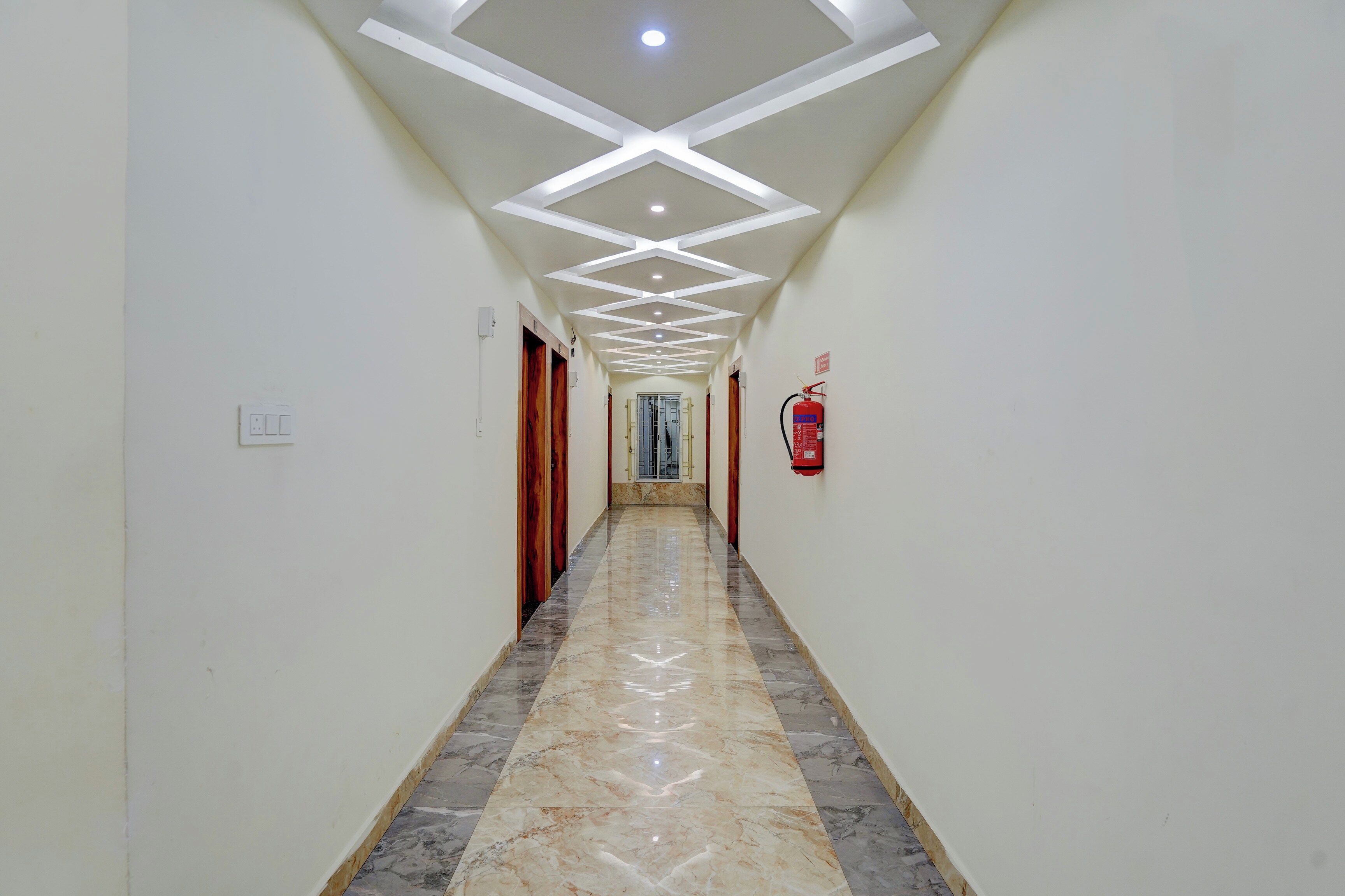A corridor with a marble floor, white walls, and a ceiling with recessed lighting.