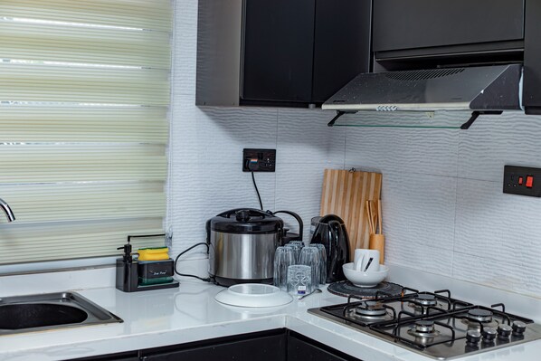 A modern kitchen with a gas stove, a coffee maker, and a kettle. - Villa De Fredwaa Unit 2 (Dar es Salaam)
