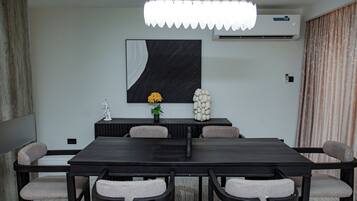 A modern conference room with a dark wooden table, six chairs, a large abstract painting, a potted plant, and a decorative white sculpture.