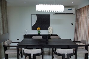 A modern conference room with a dark wooden table, six chairs, a large abstract painting, a potted plant, and a decorative white sculpture. - Villa De Fredwaa Unit 2 (Dar es Salaam)