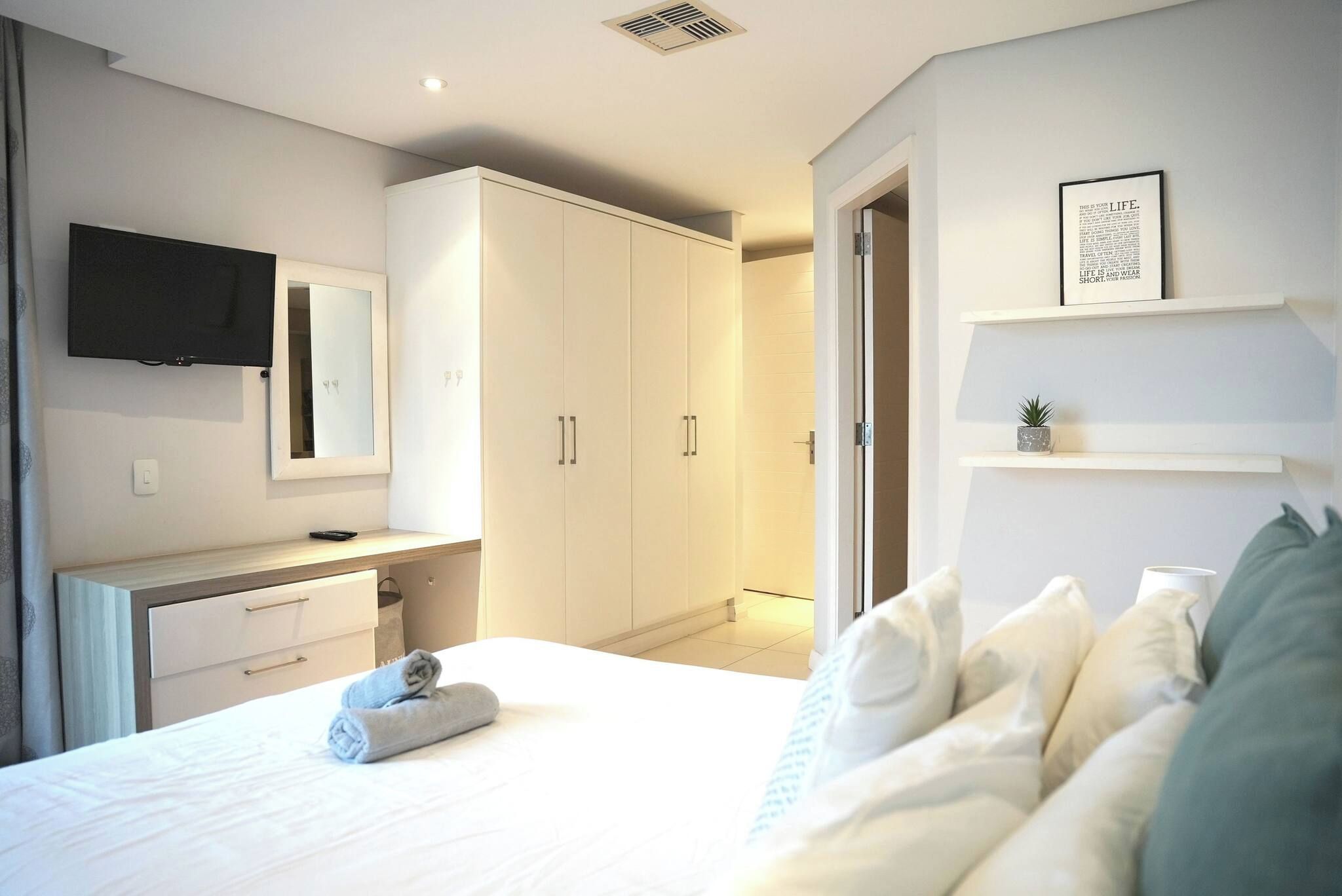 Un dormitorio moderno con una cama, una mesita de noche, un espejo, un armario y un televisor montado en la pared.