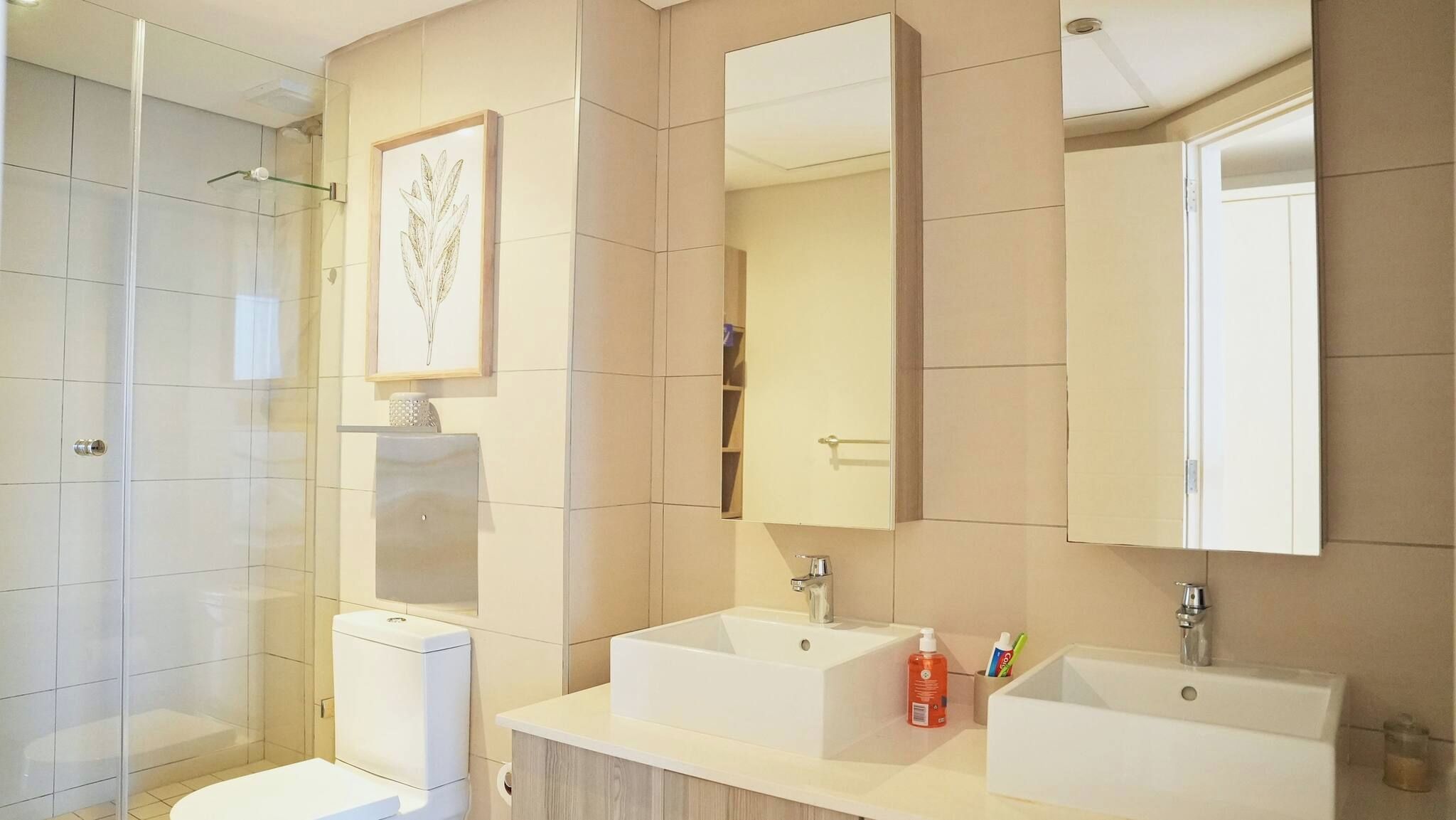 Ein modernes Badezimmer mit Duschkabine aus Glas, Toilette, zwei Waschbecken und einem Spiegel.