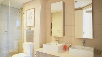 Ein modernes Badezimmer mit Duschkabine aus Glas, Toilette, zwei Waschbecken und einem Spiegel.