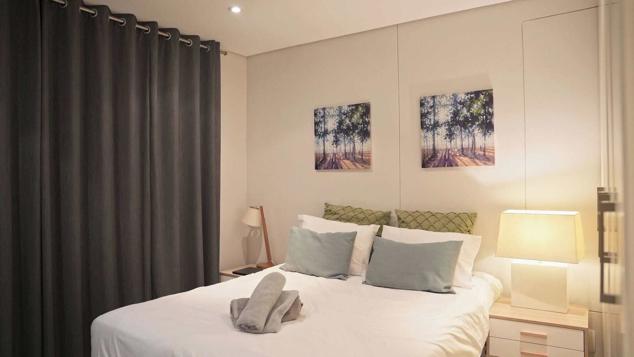 Une chambre d’hôtel avec un lit, des oreillers, une lampe de chevet, une table de chevet et deux tableaux au mur.