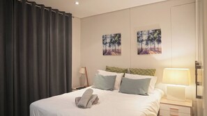 Ein Hotelzimmer mit Bett, Kissen, einer Nachttischlampe, einem Nachttisch und zwei Bildern an der Wand.