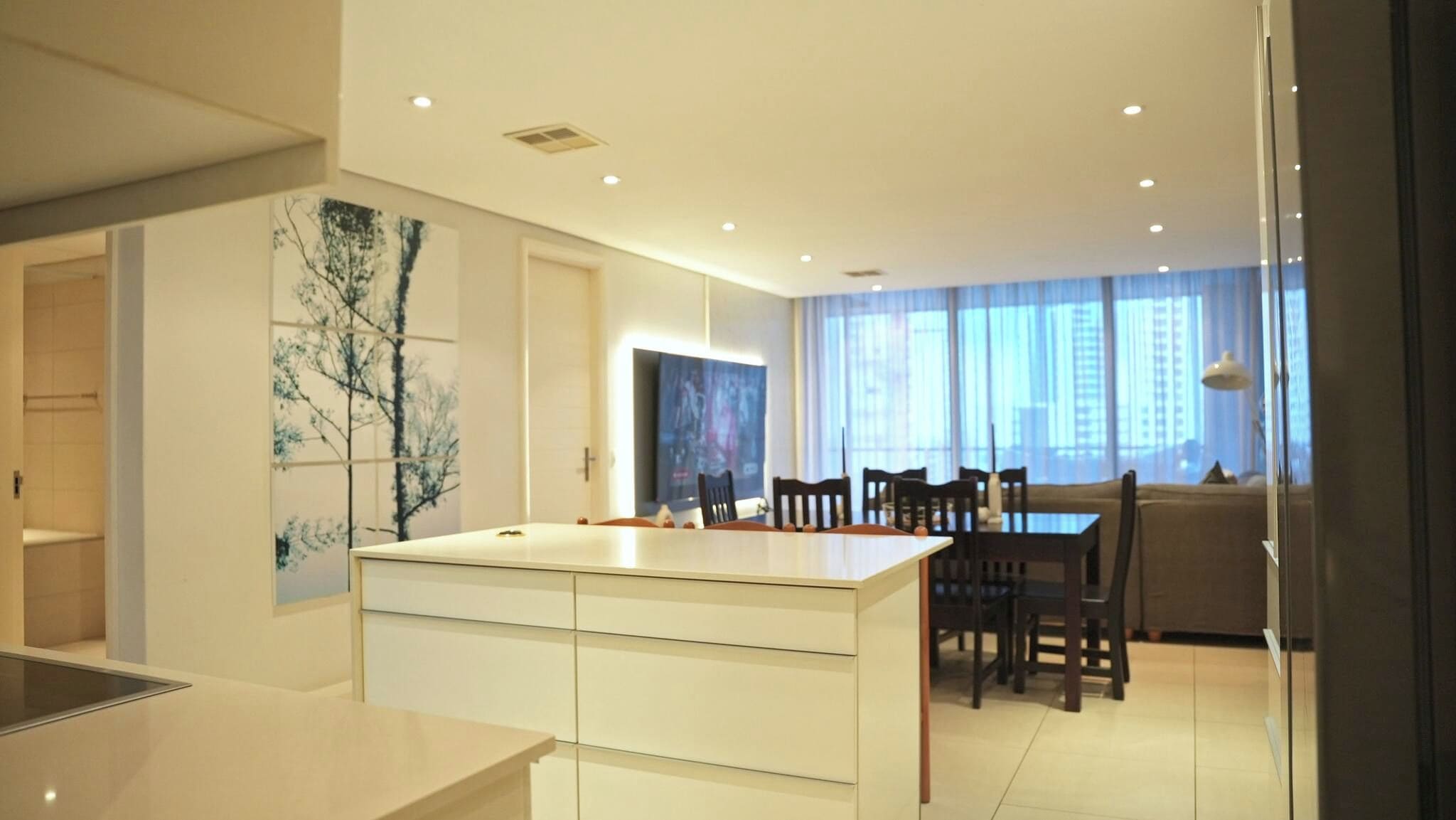 A modern kitchen with a central island, dining area with chairs, and a large window with curtains.