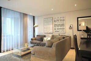 Ein modernes Wohnzimmer mit einem Glastisch, einer Couch und einem großen Fenster mit durchsichtigen Vorhängen.