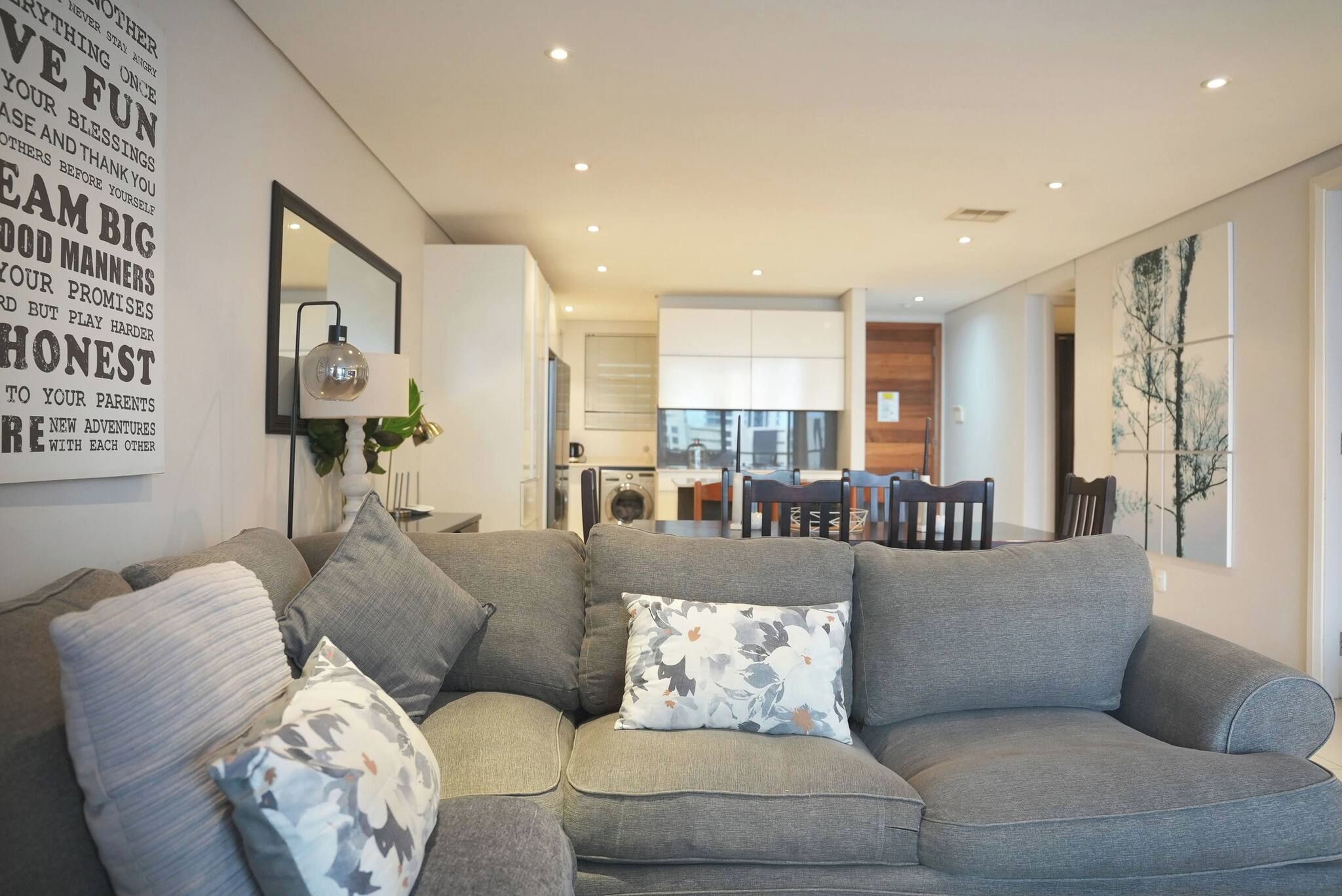 Una sala de estar moderna con un sofá seccional gris, un comedor con mesa y sillas, y una cocina al fondo.