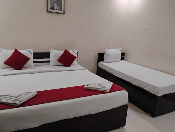 Habitación de hotel con dos camas, una más grande y otra más pequeña, ambas con ropa blanca y detalles en rojo.