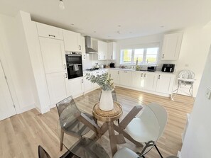A modern kitchen with white cabinets, a glass dining table, and a central vase. - Spacious 4BR Bedford Home | 6-Car Parking & Garden (Central Bedfordshire)