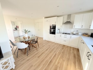 Una cocina moderna con armarios blancos, una mesa de comedor con sillas y piso de madera.