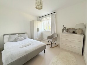 A bedroom with a bed, a chair, a dresser, and a window with curtains. - Spacious 4BR Bedford Home | 6-Car Parking & Garden (Central Bedfordshire)