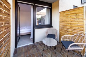 A balcony with a wicker chair and a small table, a sliding door leading to a room, and a wooden fence. - Tranquil 1-bedroom apartment in delightful Würzburg neighborhood (Würzburg)