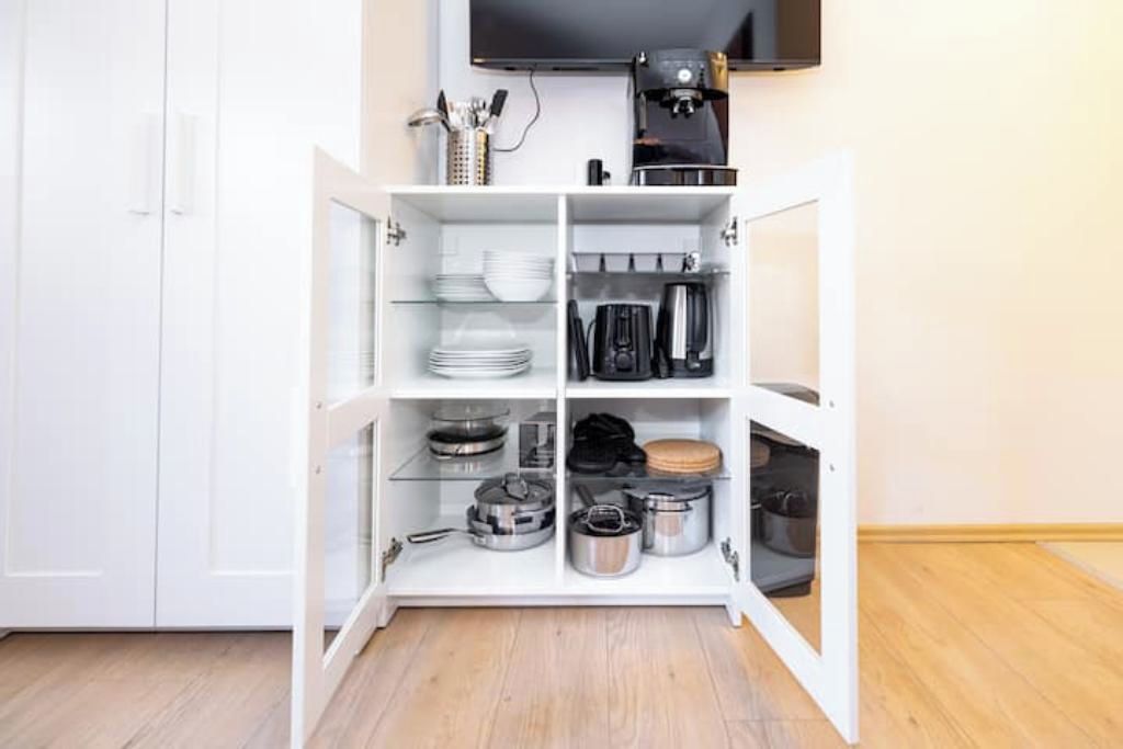 Ein weißes Schränkchen mit Regalen, das Küchenutensilien, eine Kaffeemaschine und einen Fernseher beherbergt.