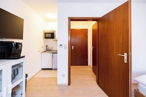 Een kleine hotelkamer met een kitchenette, een televisie en een houten garderobe.