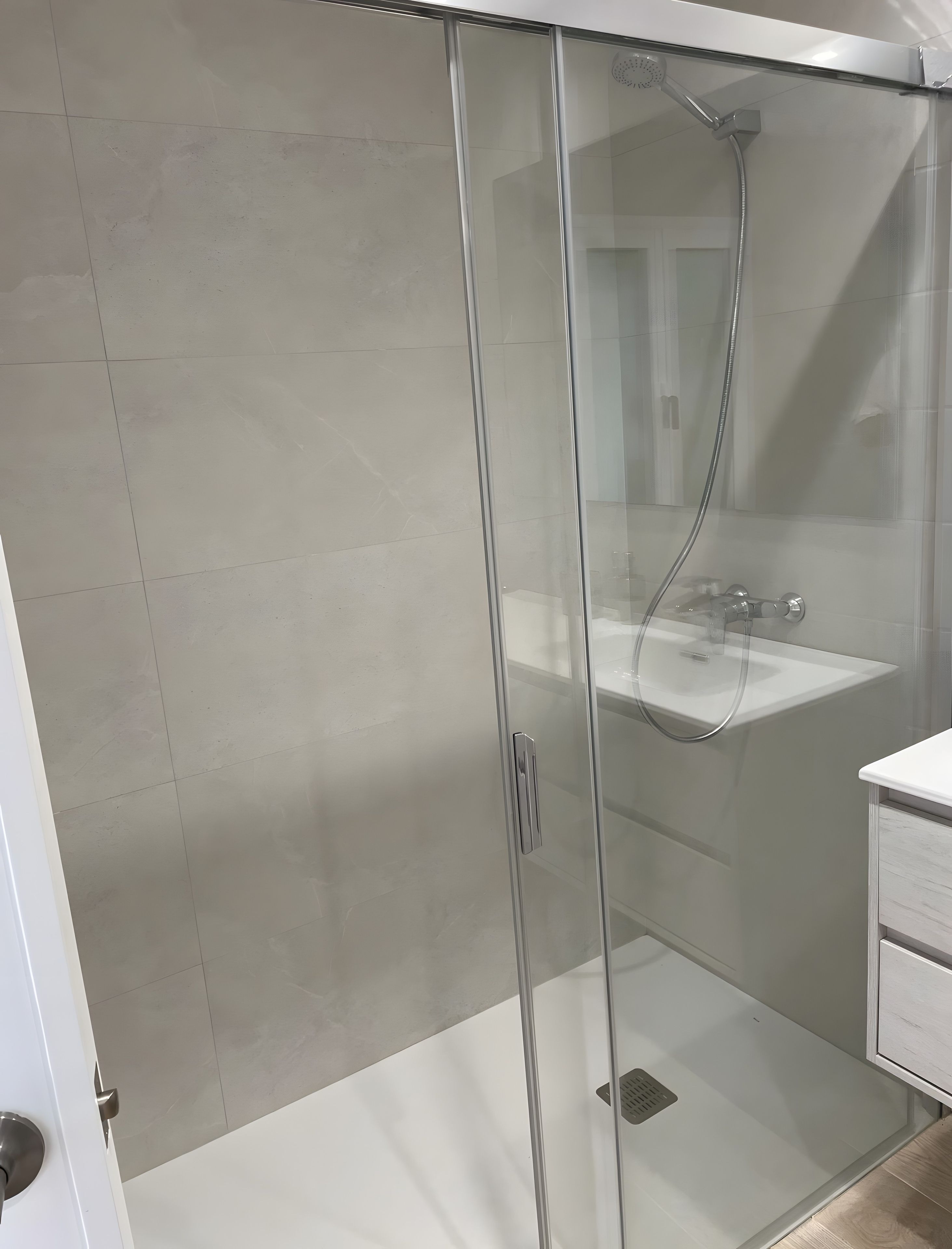 Een moderne badkamer met een douchecabine van glas, een witte wastafel en een houten vloer.