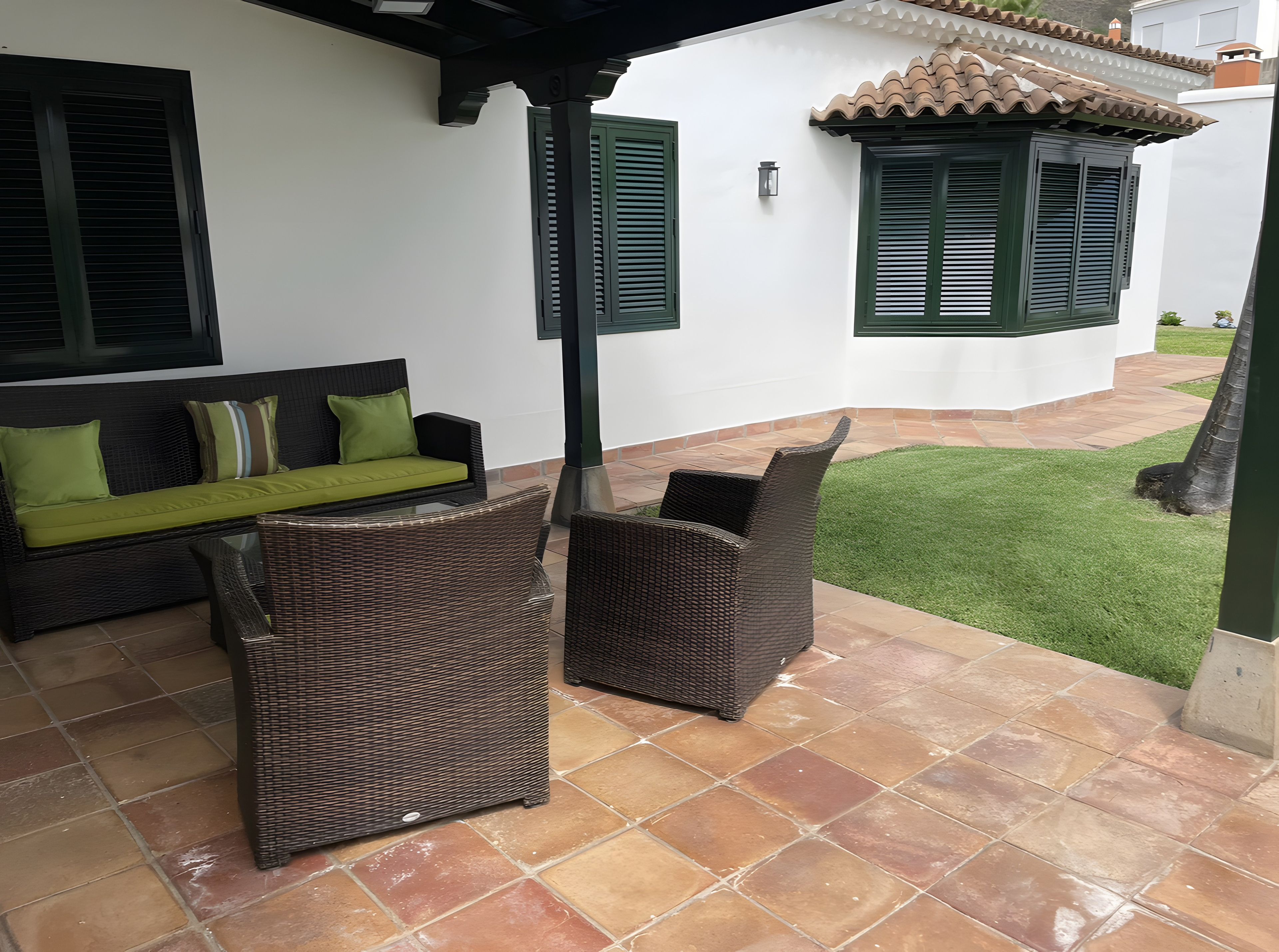 An outdoor patio with wicker furniture, a green lawn, and a white building with green shutters.