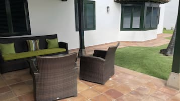 An outdoor patio with wicker furniture, a green lawn, and a white building with green shutters.