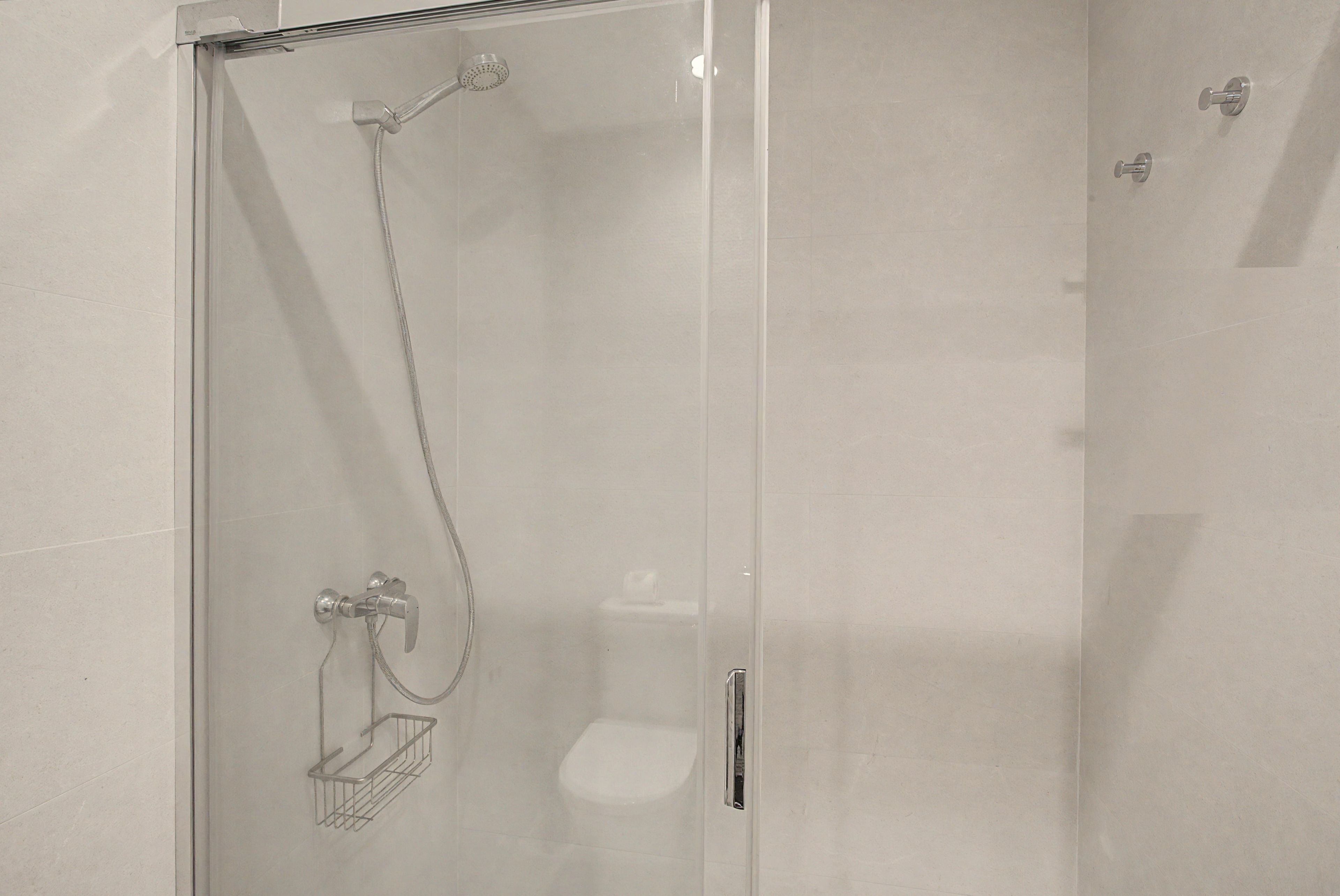 Ducha envuelta en vidrio con cabezal de ducha de mano y llave empotrada.